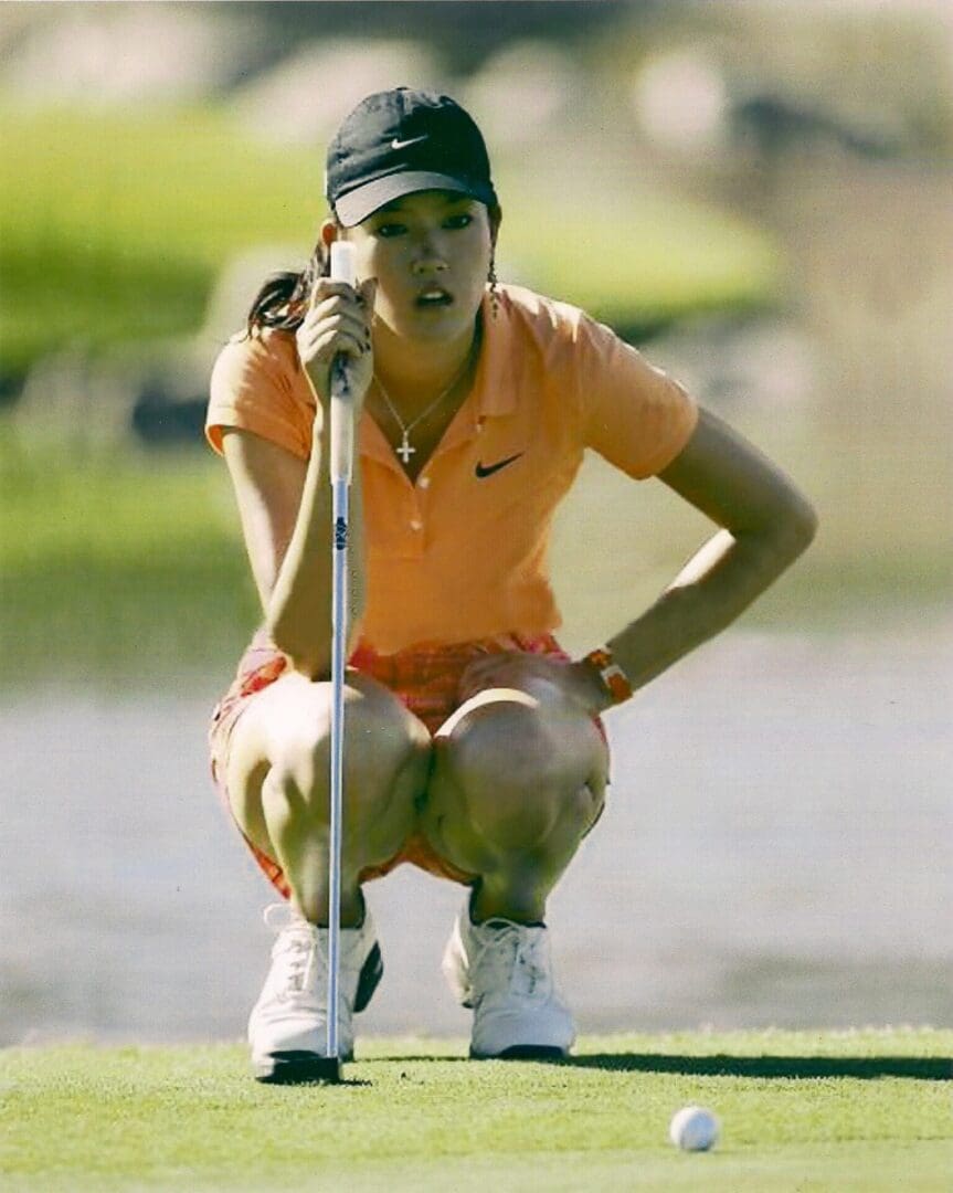 A woman crouches down on the golf course.