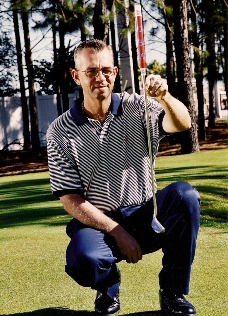 A man kneeling down on the grass holding onto a golf club.