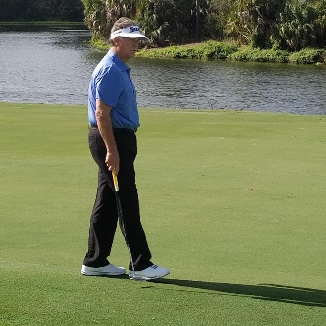 A man in blue shirt holding golf club on green.