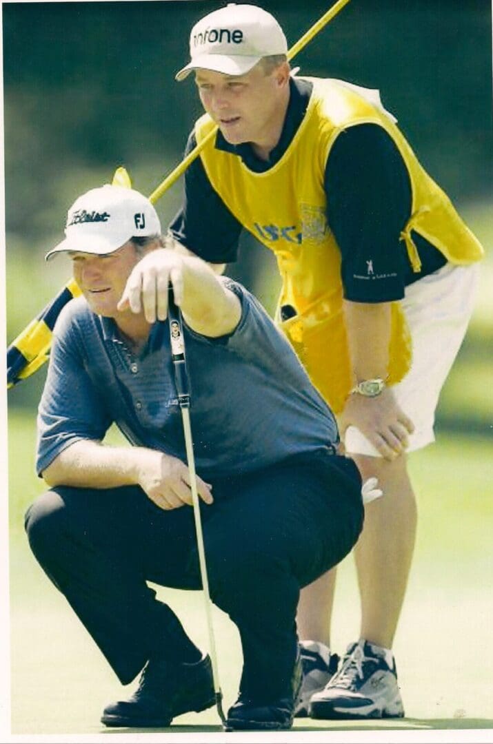 A man kneeling down next to another person holding a golf club.