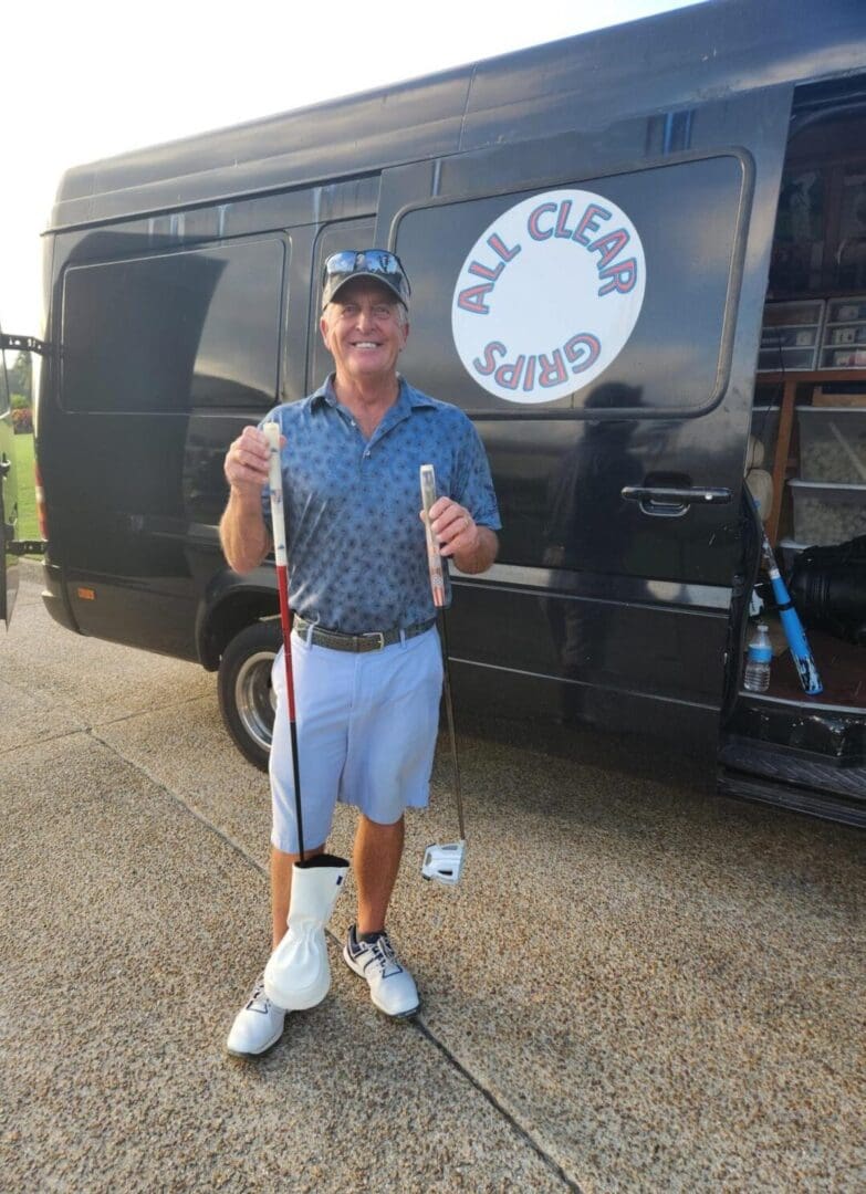 A man holding two golf clubs in front of a van.